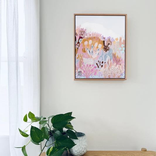 Framed abstract art on a wall above a wooden table with a plant and books.