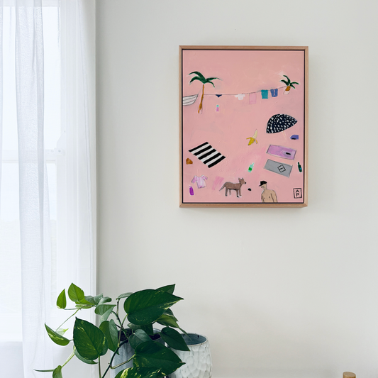Pink framed artwork on a white wall above a wooden table with a plant.