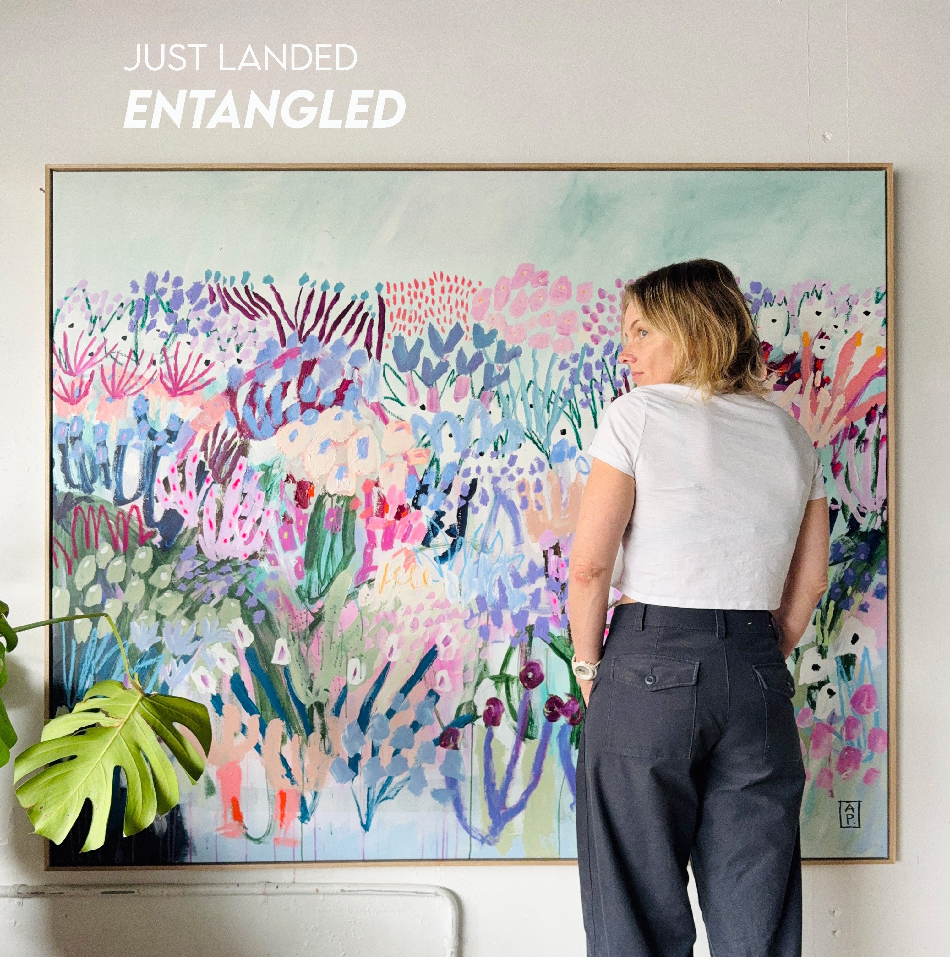 Person standing in front of a large abstract floral painting with 'Just Landed Entangled' text above.
