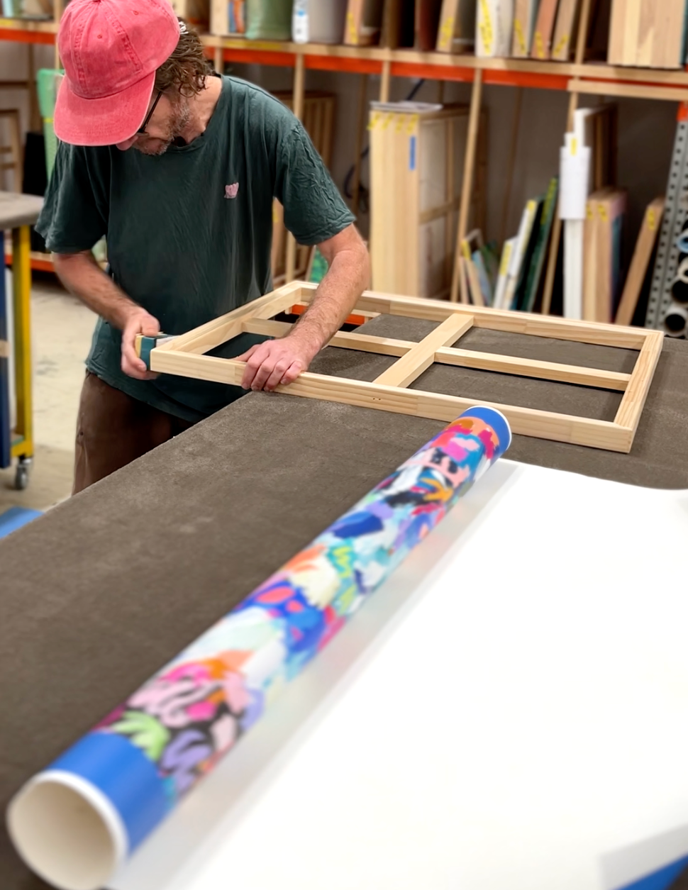 Person working on a wooden frame with a colorful roll of paper in a workshop setting.